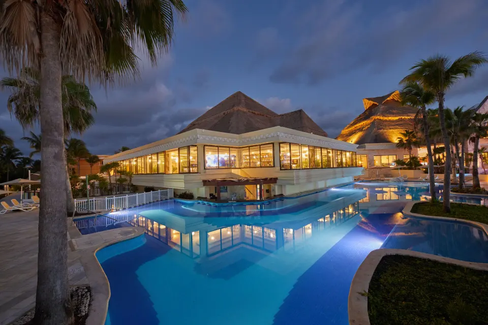 Evening view of illuminated pool and glass-walled building at Bahia Principe Luxury Akumal.