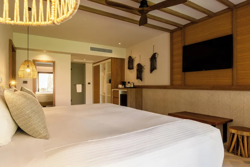 Low-angle view of a king bed and TV wall with wooden accents at Bahia Principe Luxury Akumal.