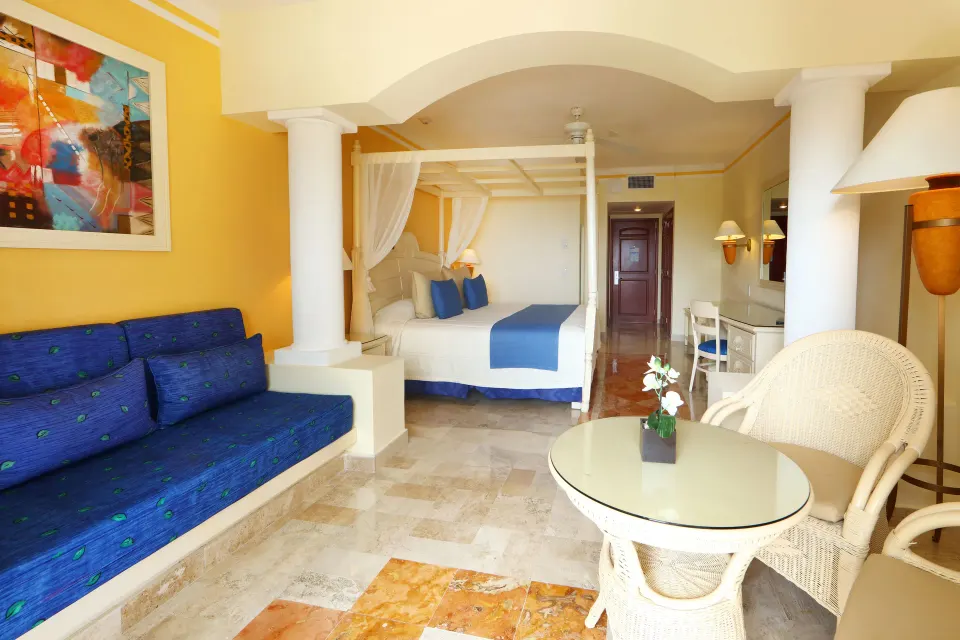 Spacious four-poster bed room with blue accents and seating at Bahia Principe Luxury Akumal
