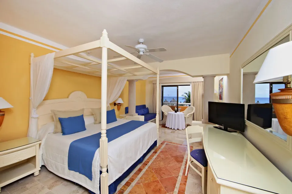 Four-poster king bed with blue throw and balcony view toward the ocean at Bahia Principe Luxury Akumal