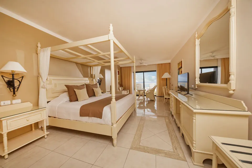Four-poster king bed and sitting area in a guest room at Bahia Principe Luxury Akumal.