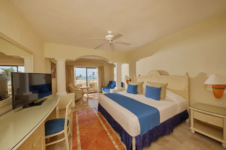 King bed with blue accents and balcony overlooking greenery at Bahia Principe Luxury Akumal.