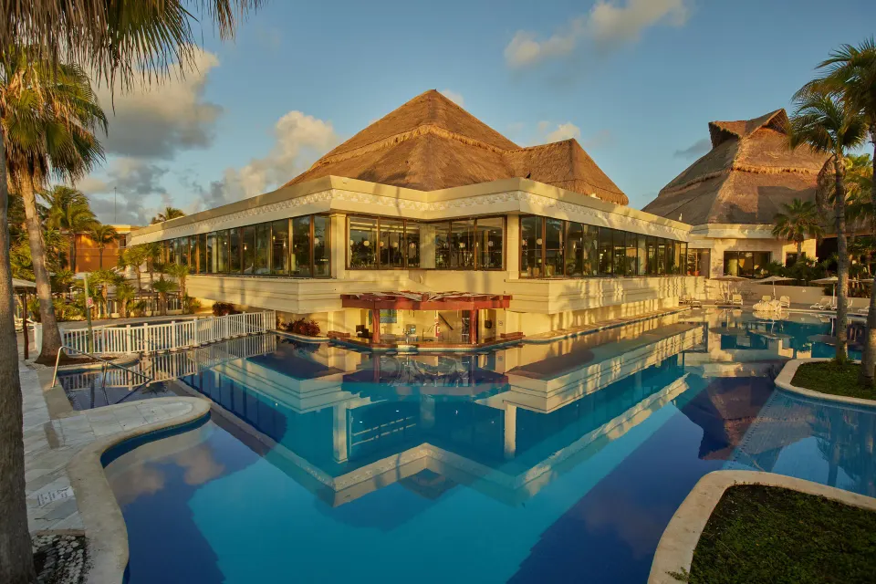 Resort pool reflecting a multi-level building with large windows at Bahia Principe Luxury Akumal