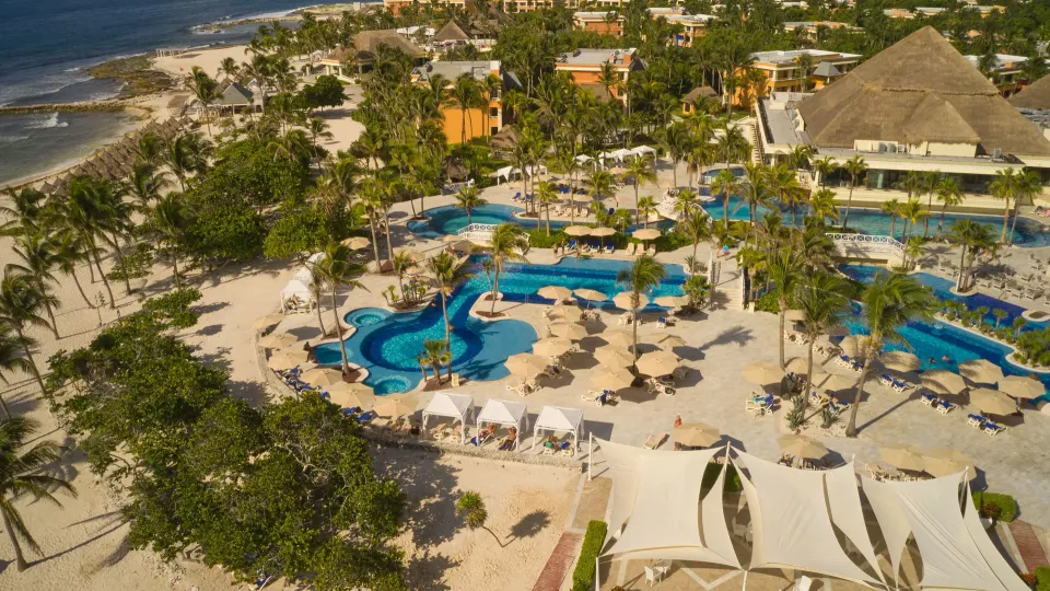 Aerial view of multiple freeform resort pools, cabanas and palm trees at Bahia Principe Luxury Akumal.