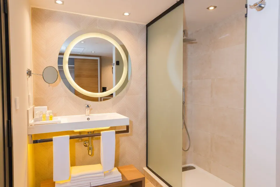 Bathroom sink and round illuminated mirror next to walk-in shower at Bahia Principe Luxury Akumal