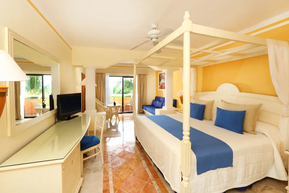 Four-poster king bed with blue accents and balcony doors in a bright room at Bahia Principe Luxury Akumal.