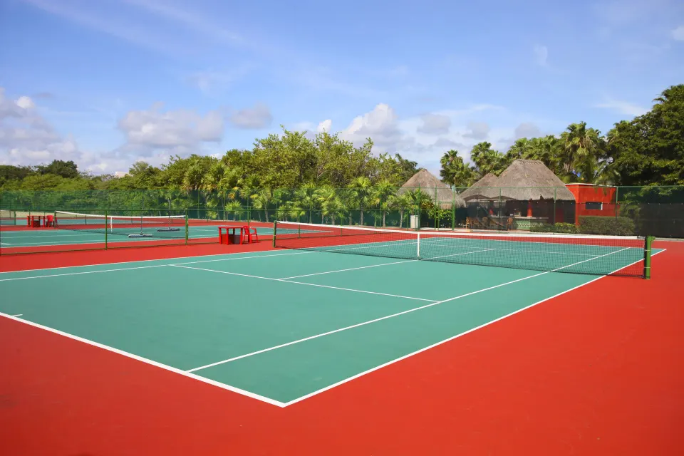 Red-and-green tennis courts framed by trees and palapa shelters at Bahia Principe Luxury Akumal