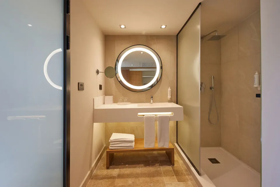 Vanity with towels and a rainfall shower visible through frosted glass at Bahia Principe Luxury Akumal