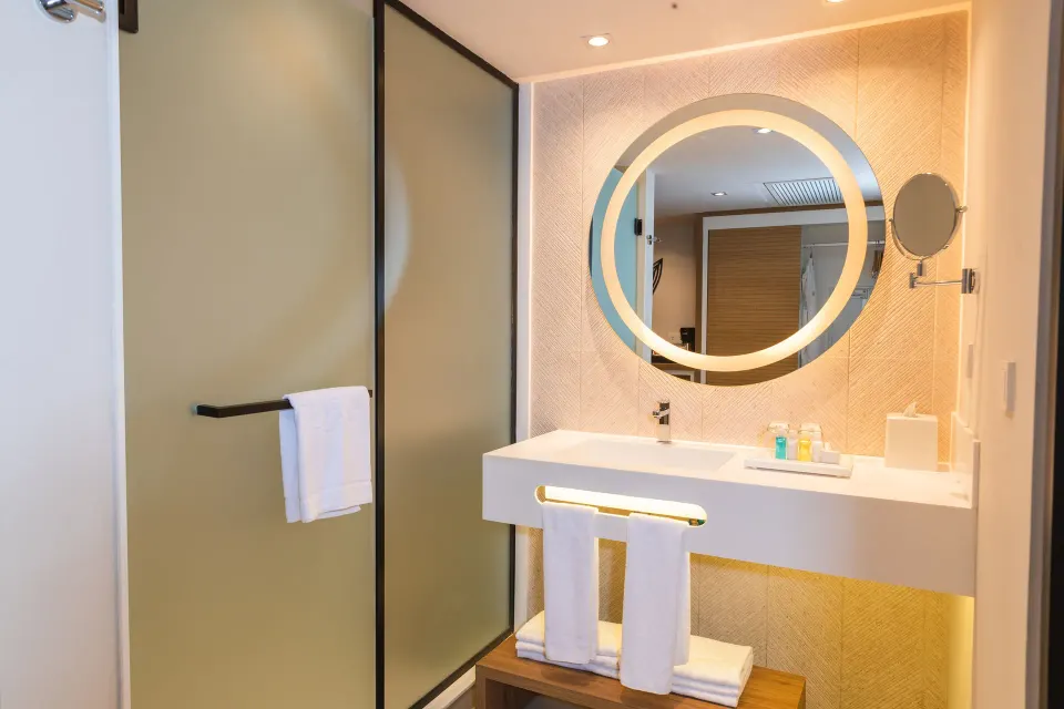 Illuminated bathroom vanity with round mirror and frosted glass shower at Bahia Principe Luxury Akumal