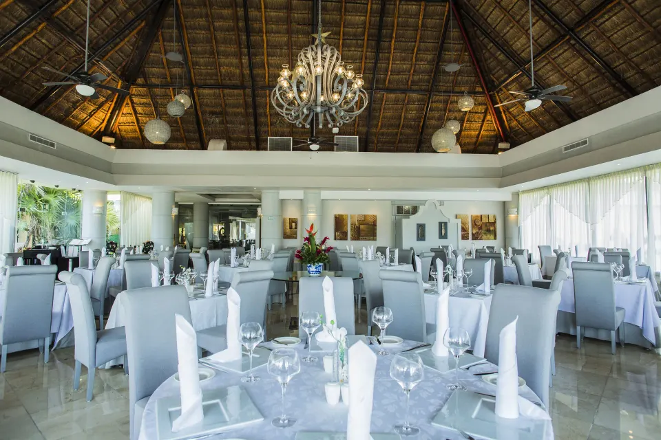 Bright palapa dining room with white-covered tables at Bahia Principe Luxury Akumal
