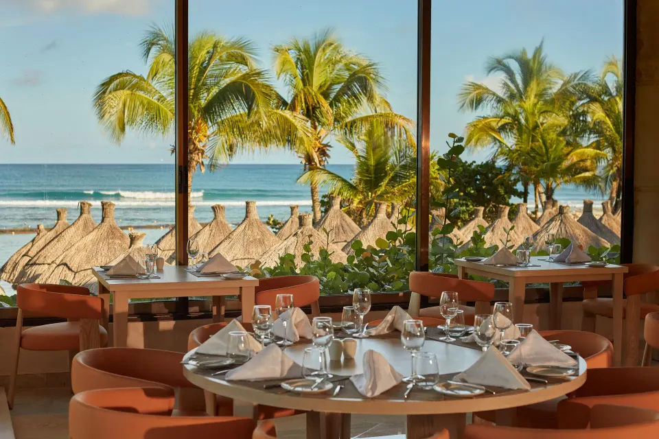Table set by a window with view of palm trees, palapas and the ocean at Bahia Principe Luxury Akumal