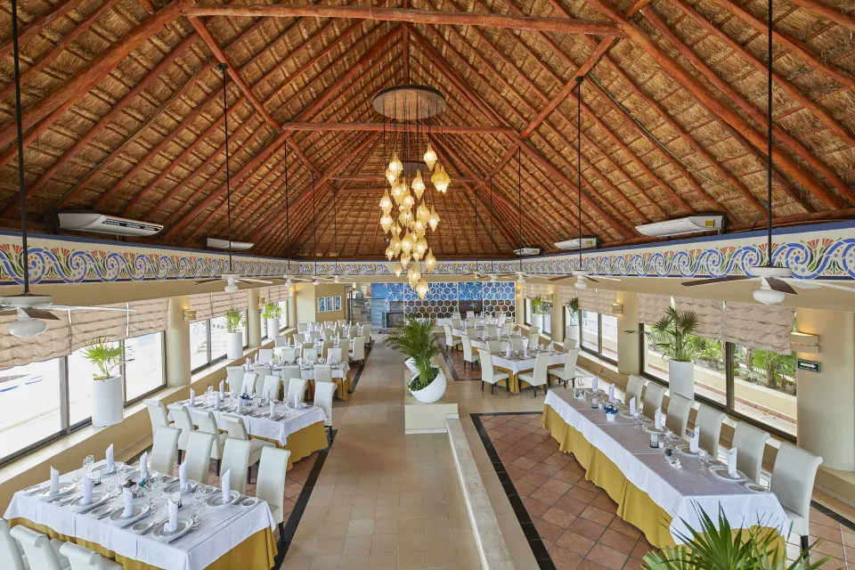 Large palapa dining room with chandeliers and long tables at Bahia Principe Luxury Akumal