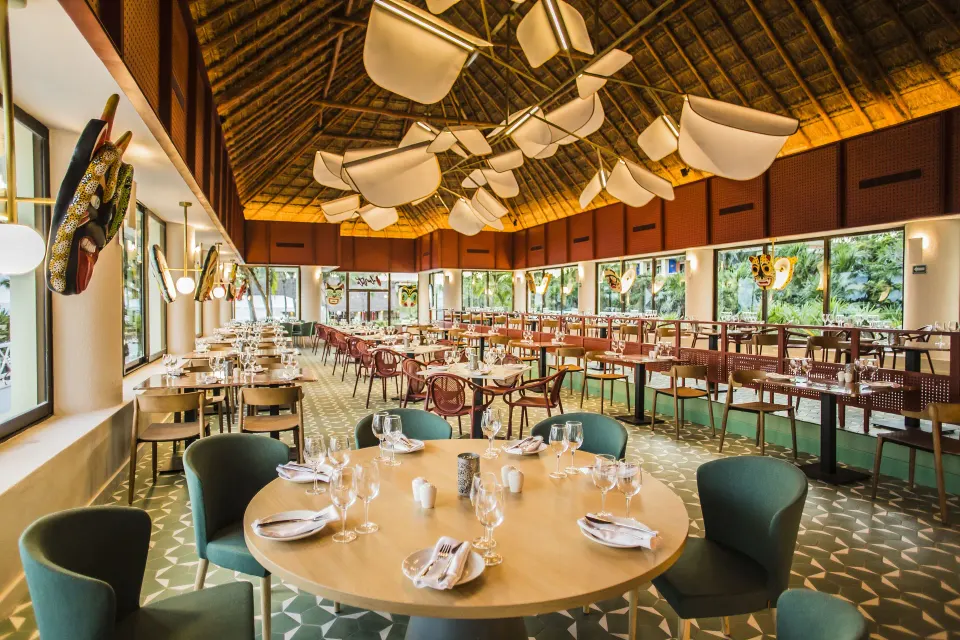 Round table set for dinner in a palapa-roofed restaurant at Bahia Principe Luxury Akumal
