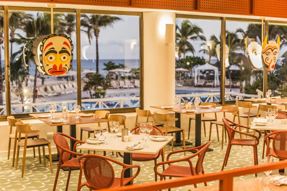 Ground-floor dining tables with ocean view and decorative masks at Bahia Principe Luxury Akumal