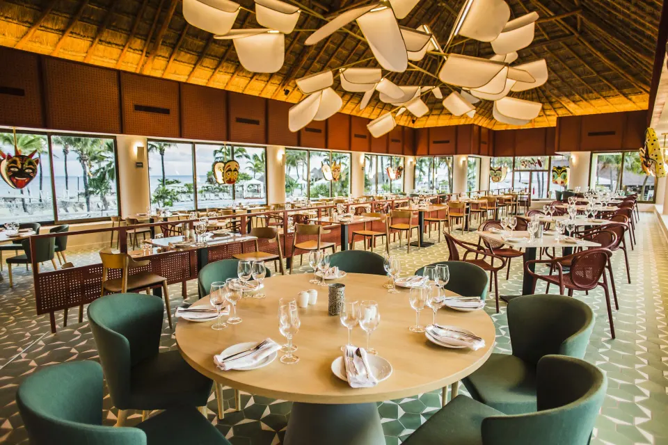 Large indoor restaurant with round tables and green chairs overlooking the beach at Bahia Principe Luxury Akumal