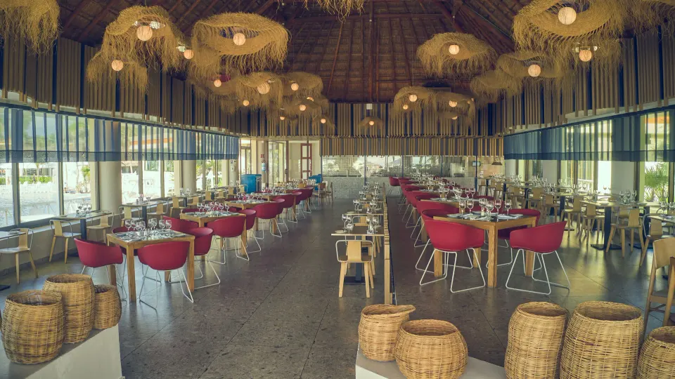 Wide dining room under a large thatch roof with hanging woven lights at Bahia Principe Luxury Akumal