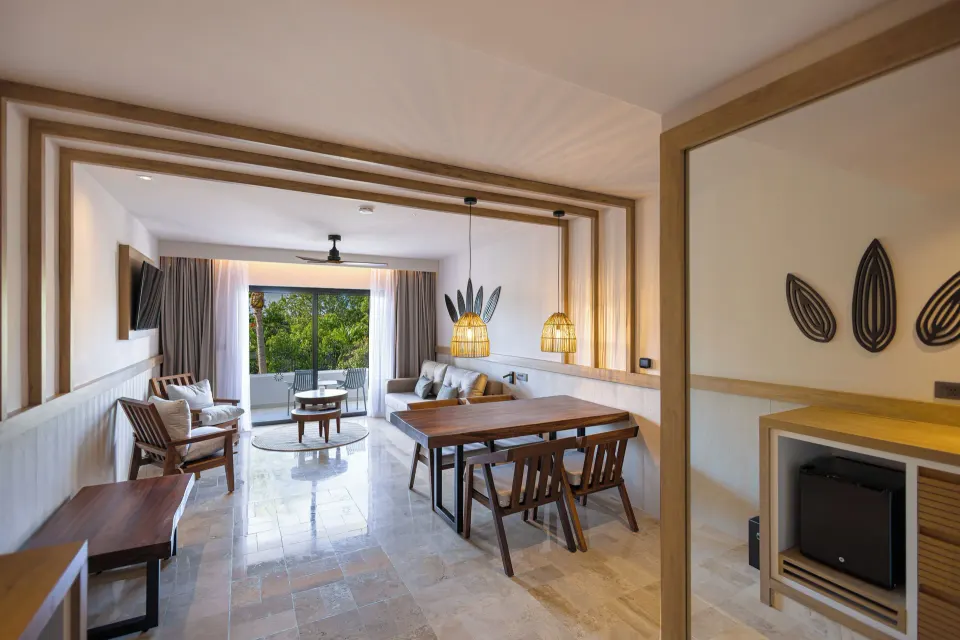 Family Suite with king bed, dining table and balcony view of greenery at Bahia Principe Luxury Akumal