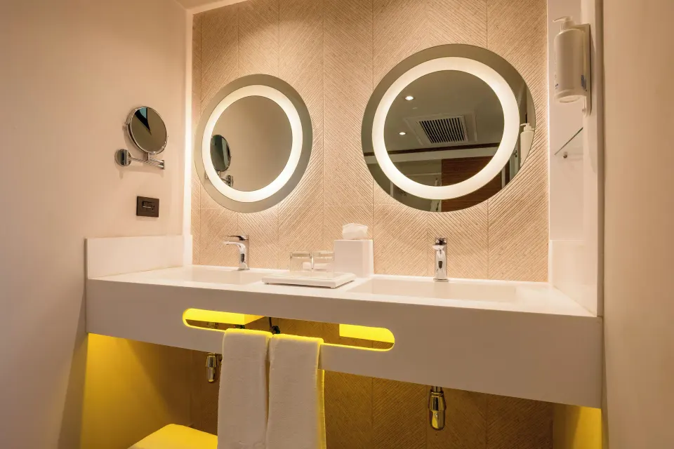 Angled view of the bathroom vanity with towels and illuminated mirrors in a two‑bedroom suite at Bahia Principe Luxury Akumal