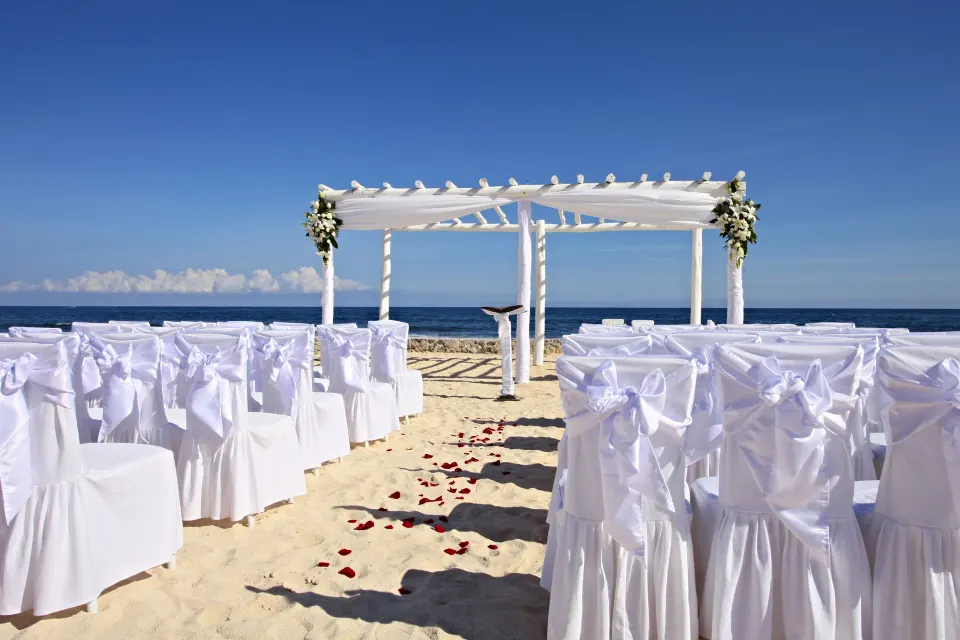 White-chairs and floral-decor arch set for a beach wedding at Bahia Principe Luxury Akumal.