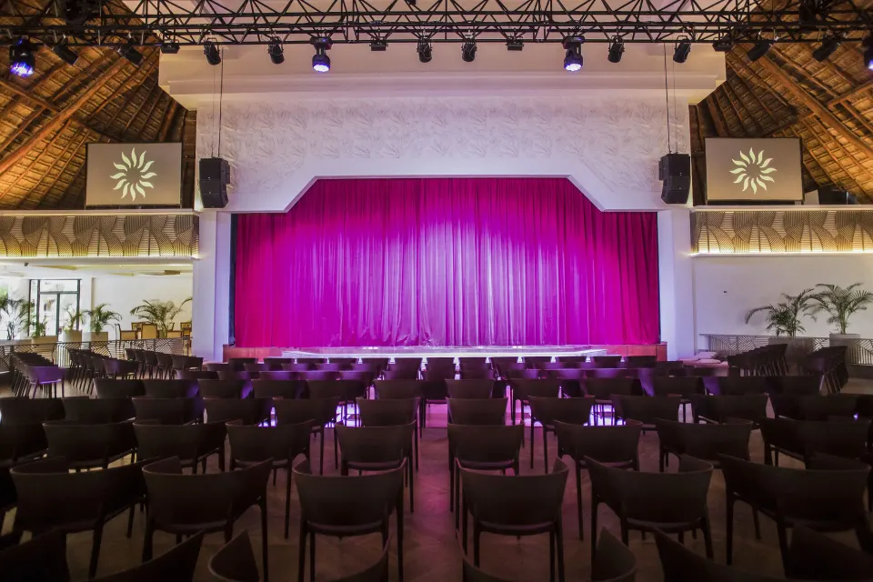 Front-facing stage with purple-pink curtain and audience chairs at Bahia Principe Luxury Akumal