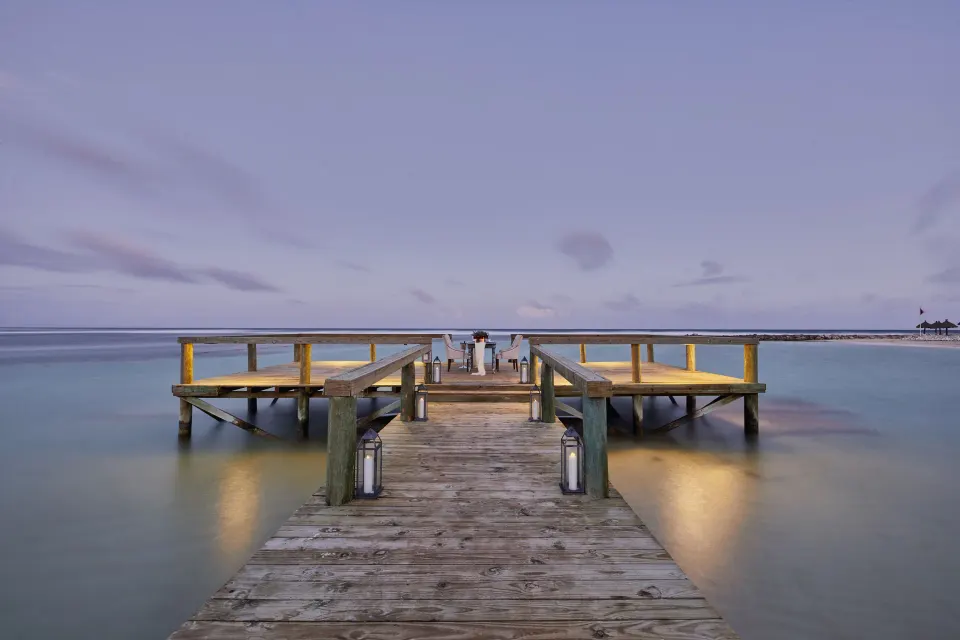 Wooden pier stretching into calm water with a small dining table at the end at Bahia Principe Luxury Akumal.