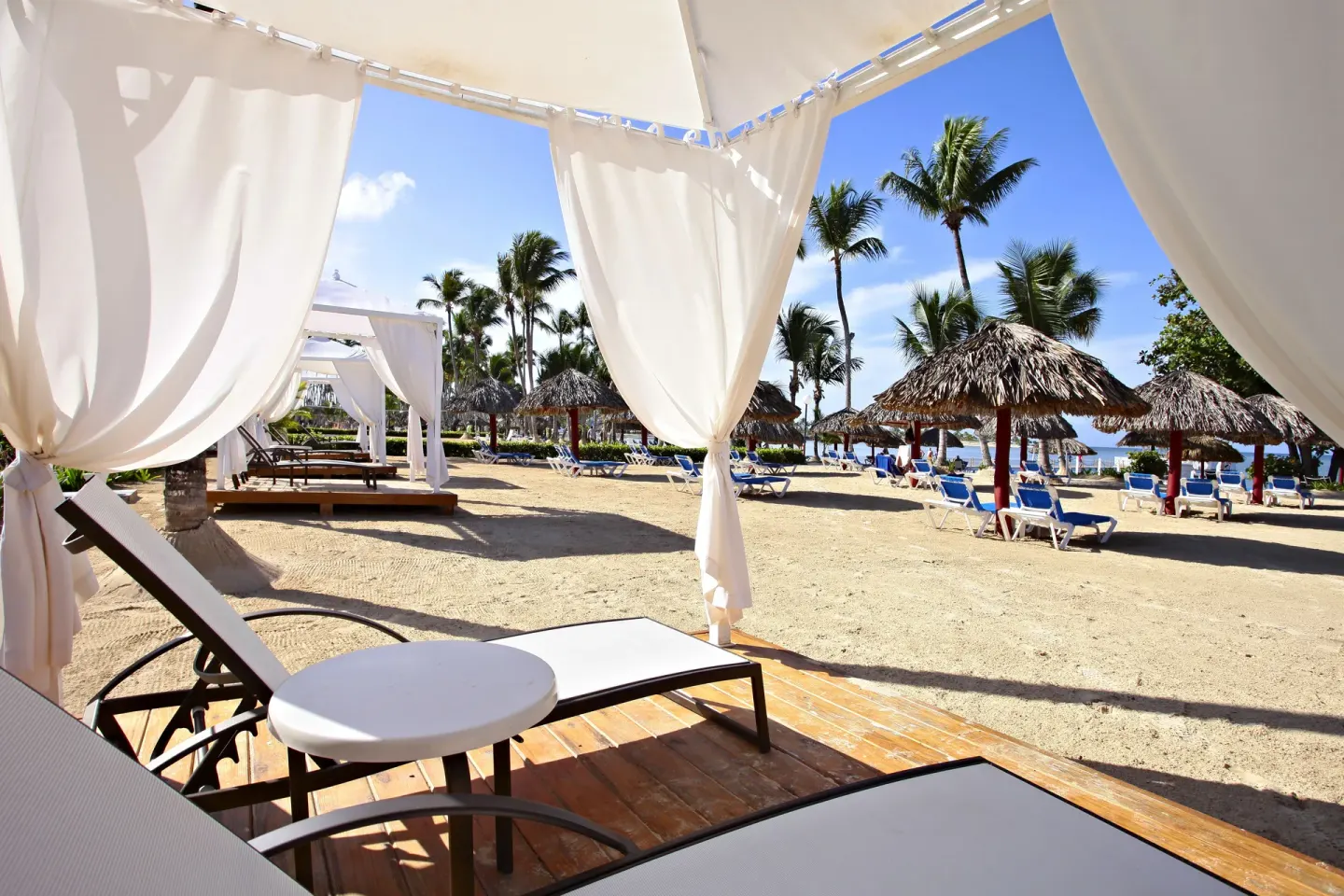 White beach cabana with loungers and palapa umbrellas at Bahia Principe Luxury Bouganville.