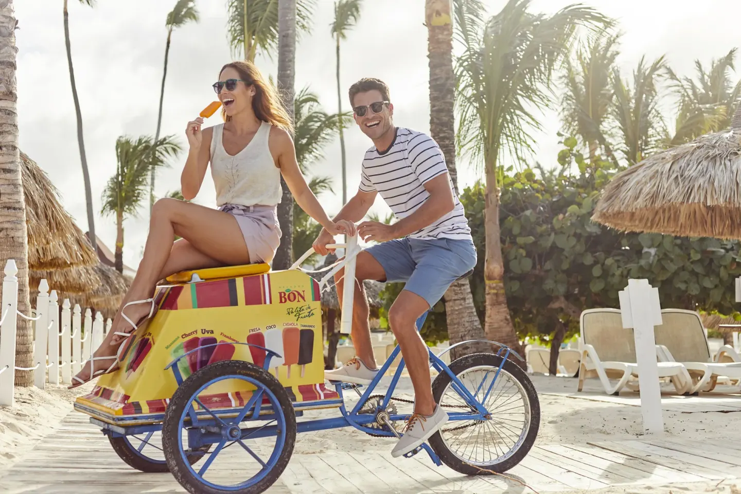 Couple posing with a colorful ice pop cart near the beach at Bahia Principe Luxury Bouganville.
