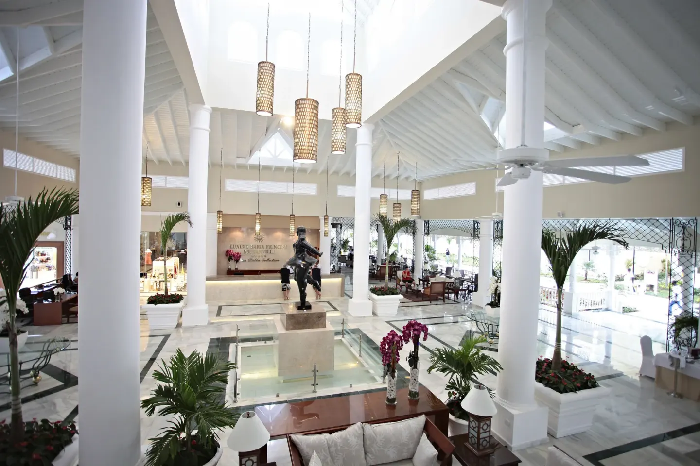 Bright lobby with white columns and a central statue at Bahia Principe Luxury Bouganville.