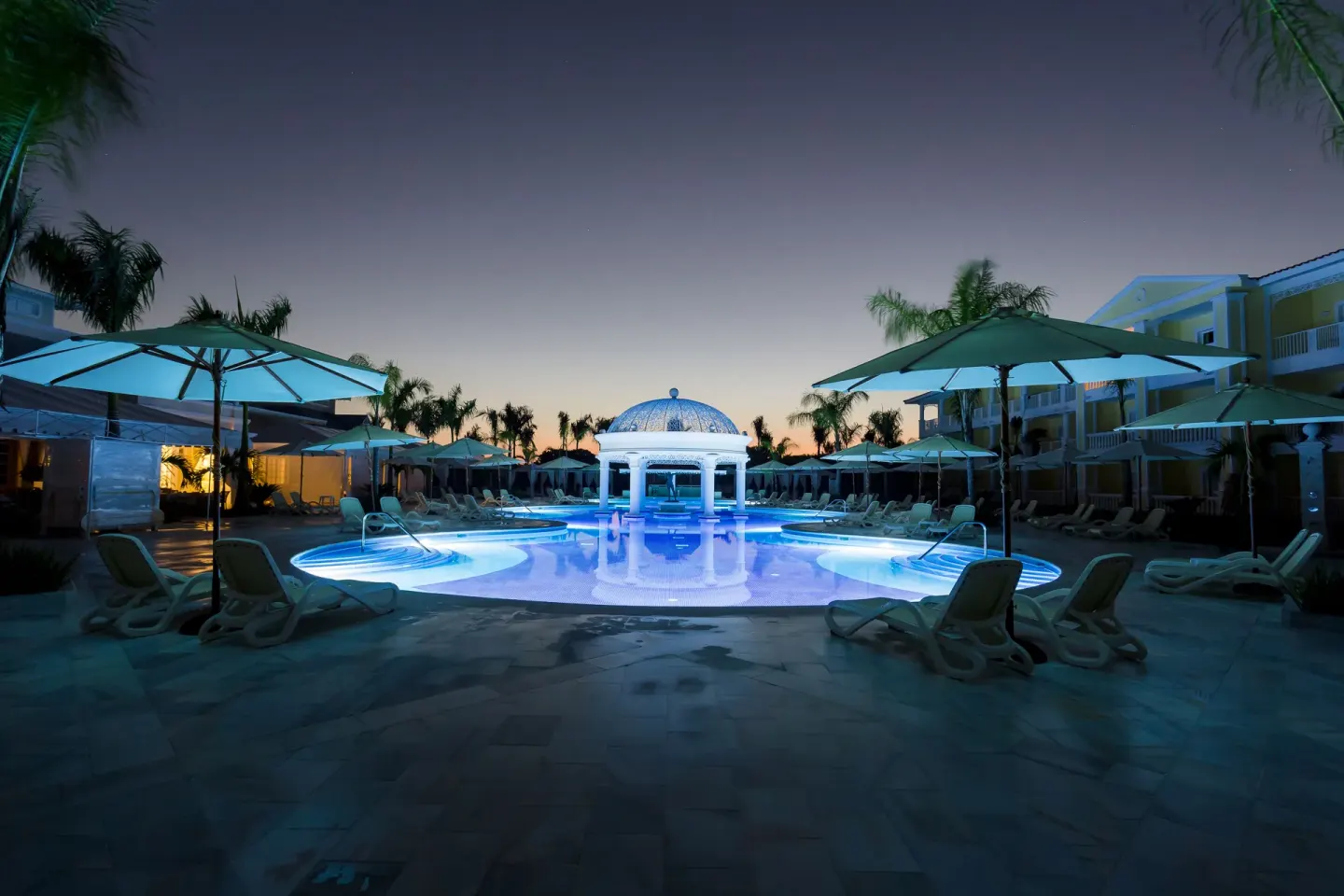 Illuminated pool deck at dusk at Bahia Principe Luxury Bouganville.