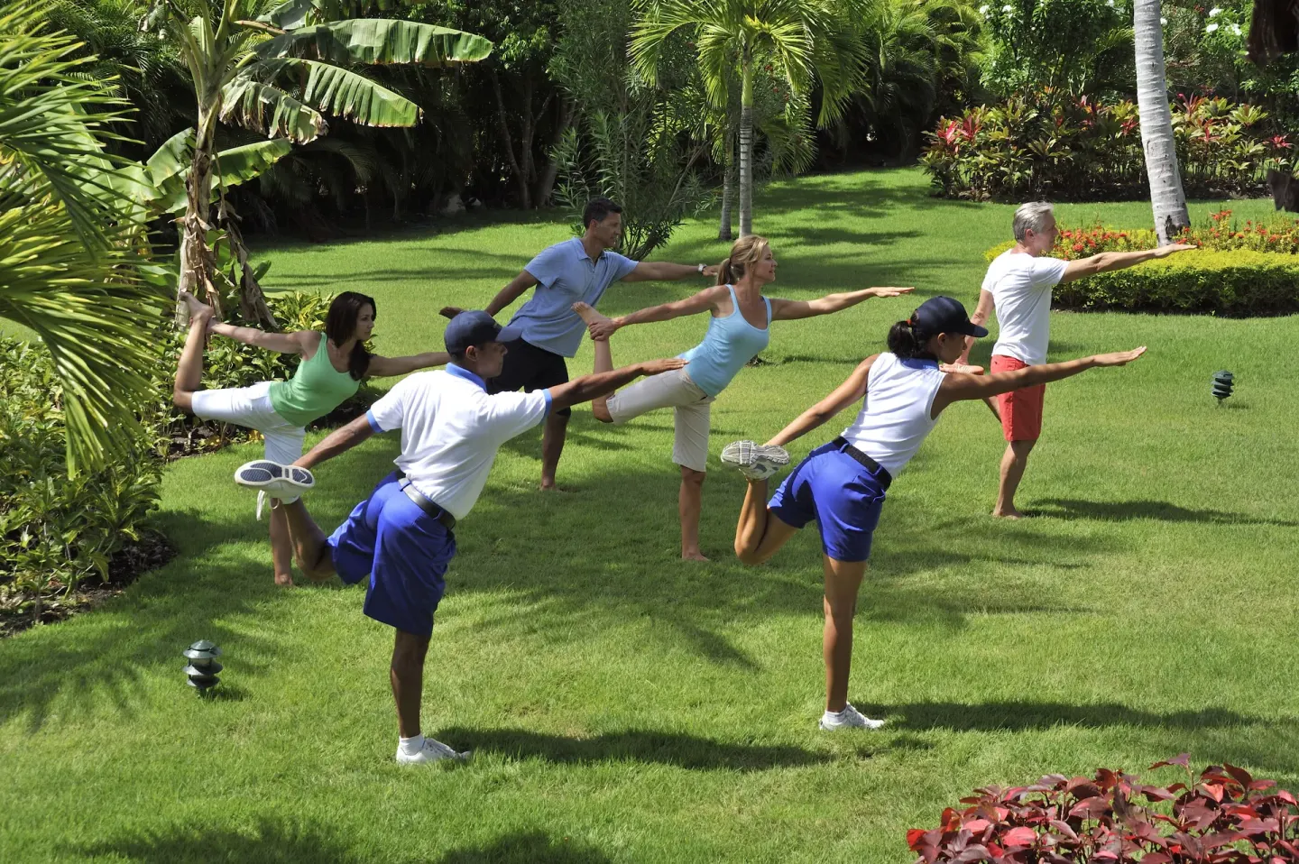 Guests stretch on a tropical lawn during a fitness class at Bahia Principe Luxury Bouganville.