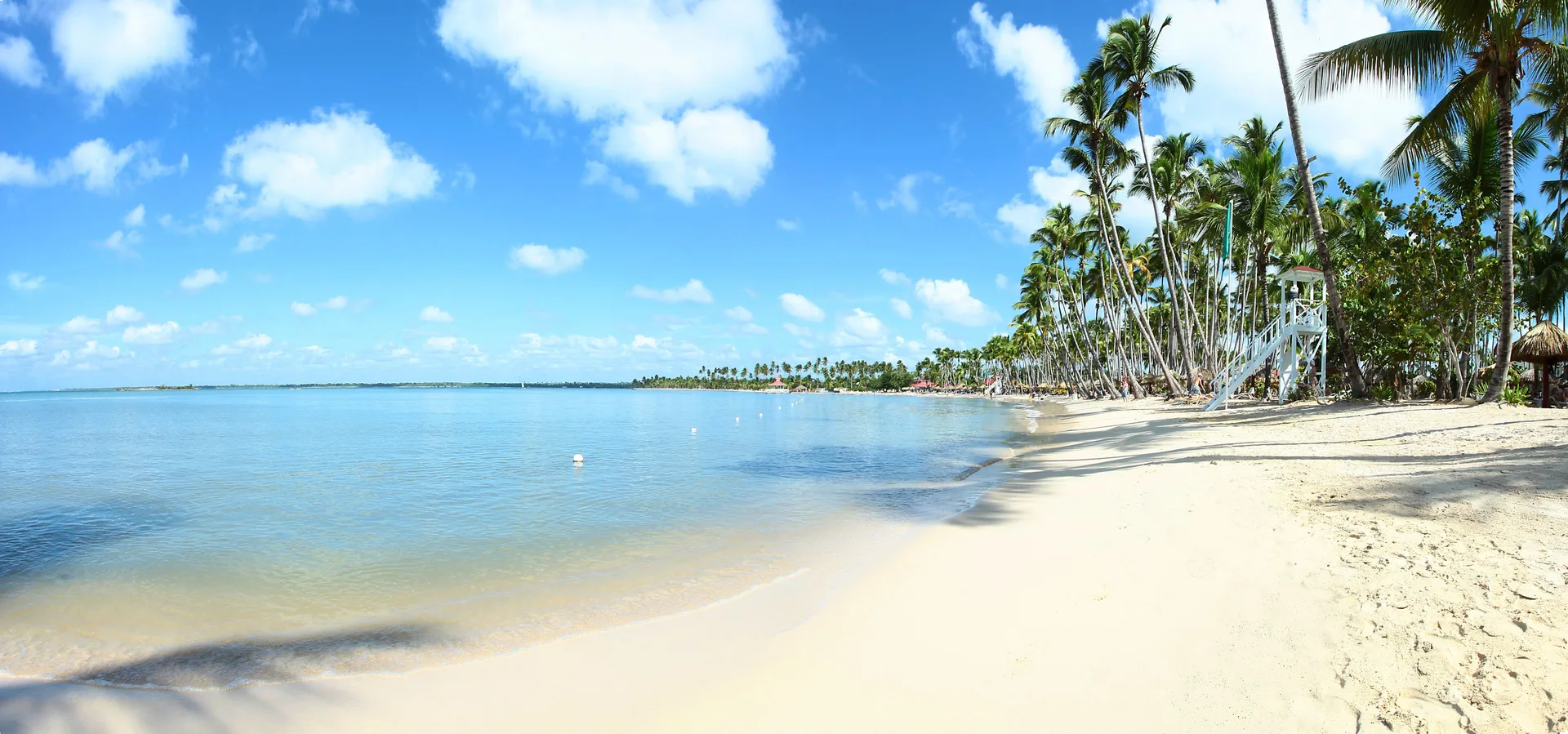 Calm sandy beach with palm trees and blue water at Bahia Principe Luxury Bouganville.