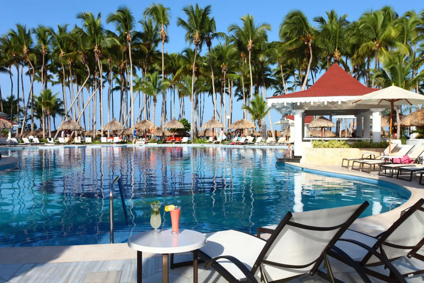 Poolside loungers, drinks, palms, and thatched shades at Bahia Principe Luxury Bouganville.