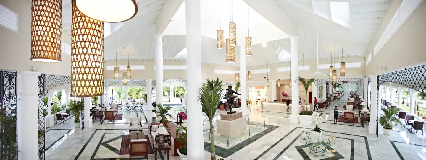 Wide lobby panorama with white columns and hanging lights at Bahia Principe Luxury Bouganville.