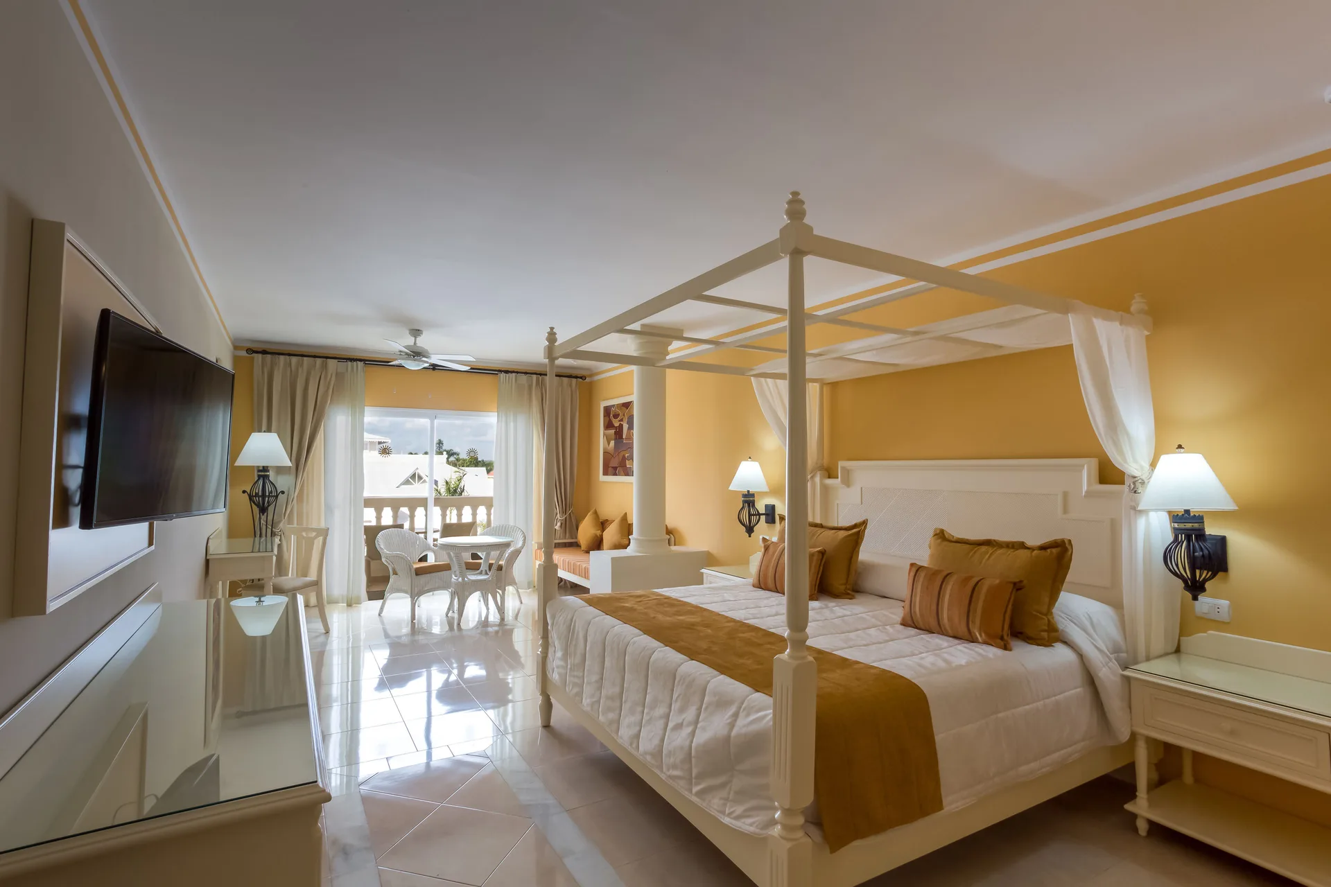 Junior Suite deluxe with canopy bed, TV, and balcony seating at Bahia Principe Luxury Bouganville.