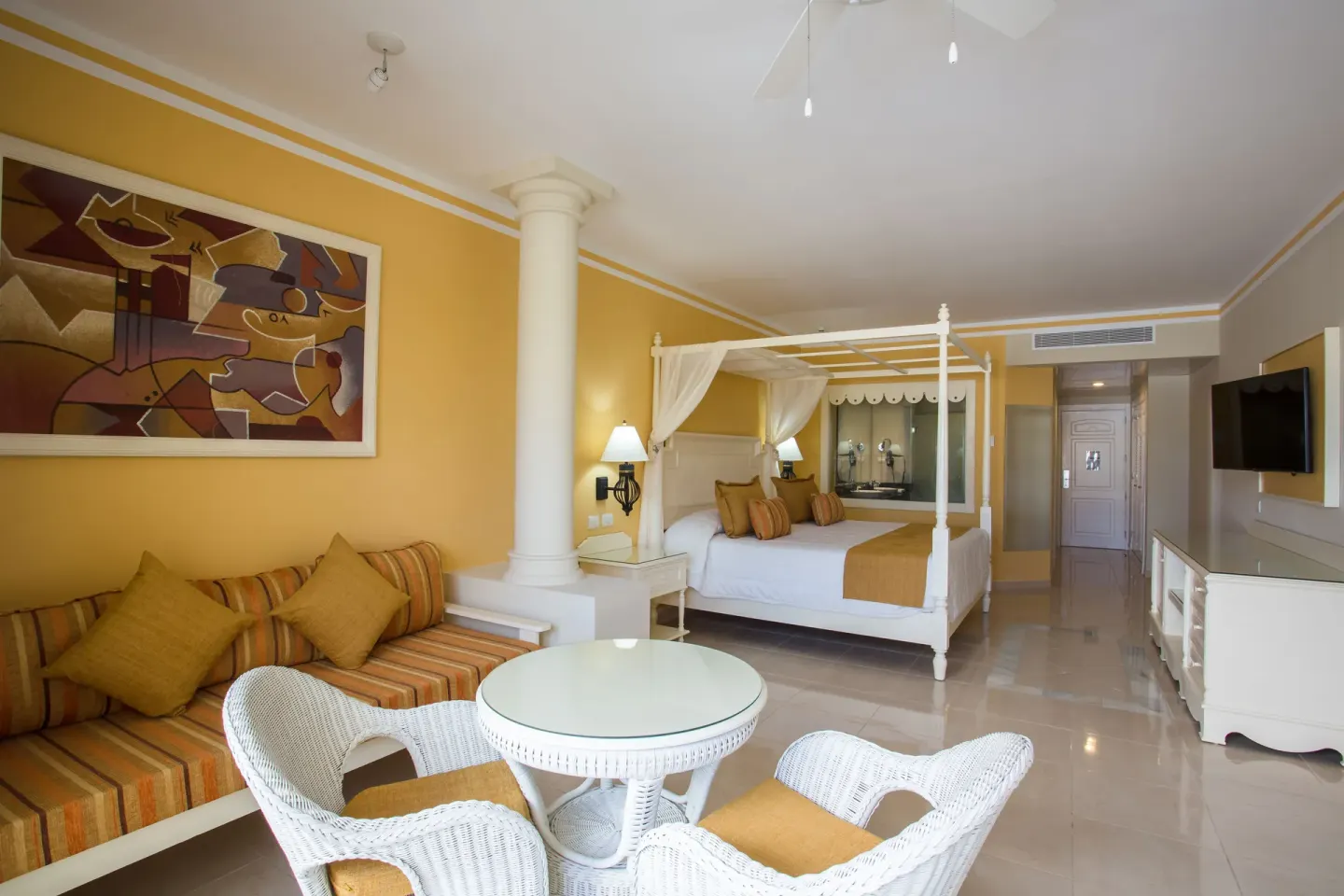 Junior Suite deluxe seating area with canopy bed in the background at Bahia Principe Luxury Bouganville.
