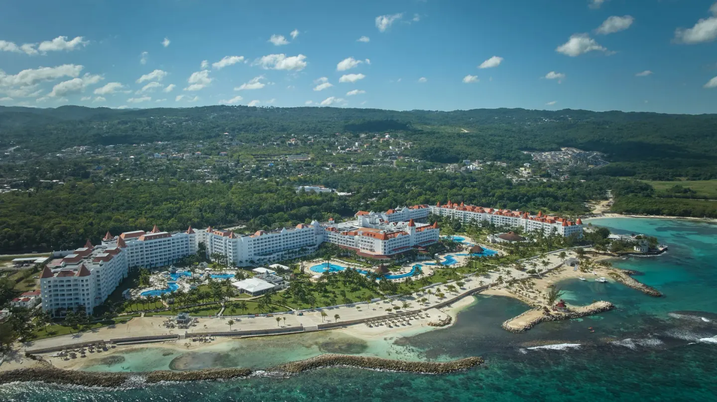 Aerial view of Bahia Principe Luxury Runaway Bay with pools, beach, and green hills.
