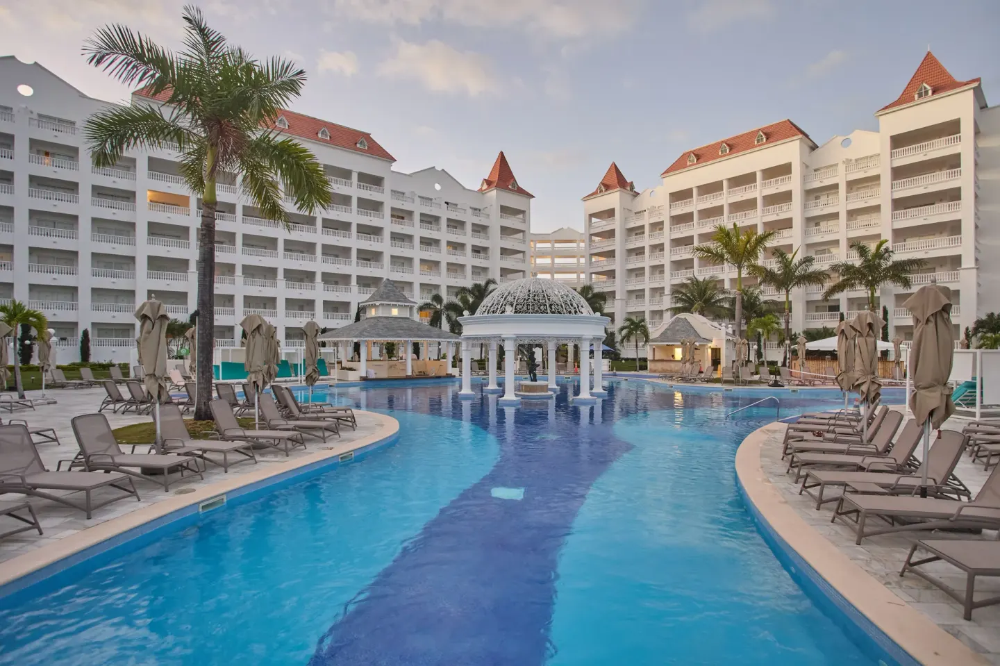 Main pool with lounge chairs, palms and white resort buildings at Bahia Principe Luxury Runaway Bay.