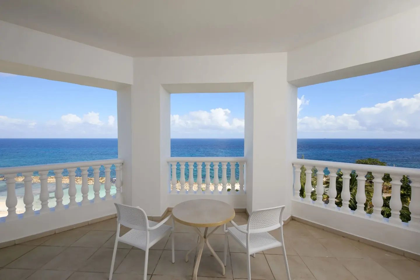 Covered balcony with table, chairs, and ocean view at Bahia Principe Luxury Runaway Bay.