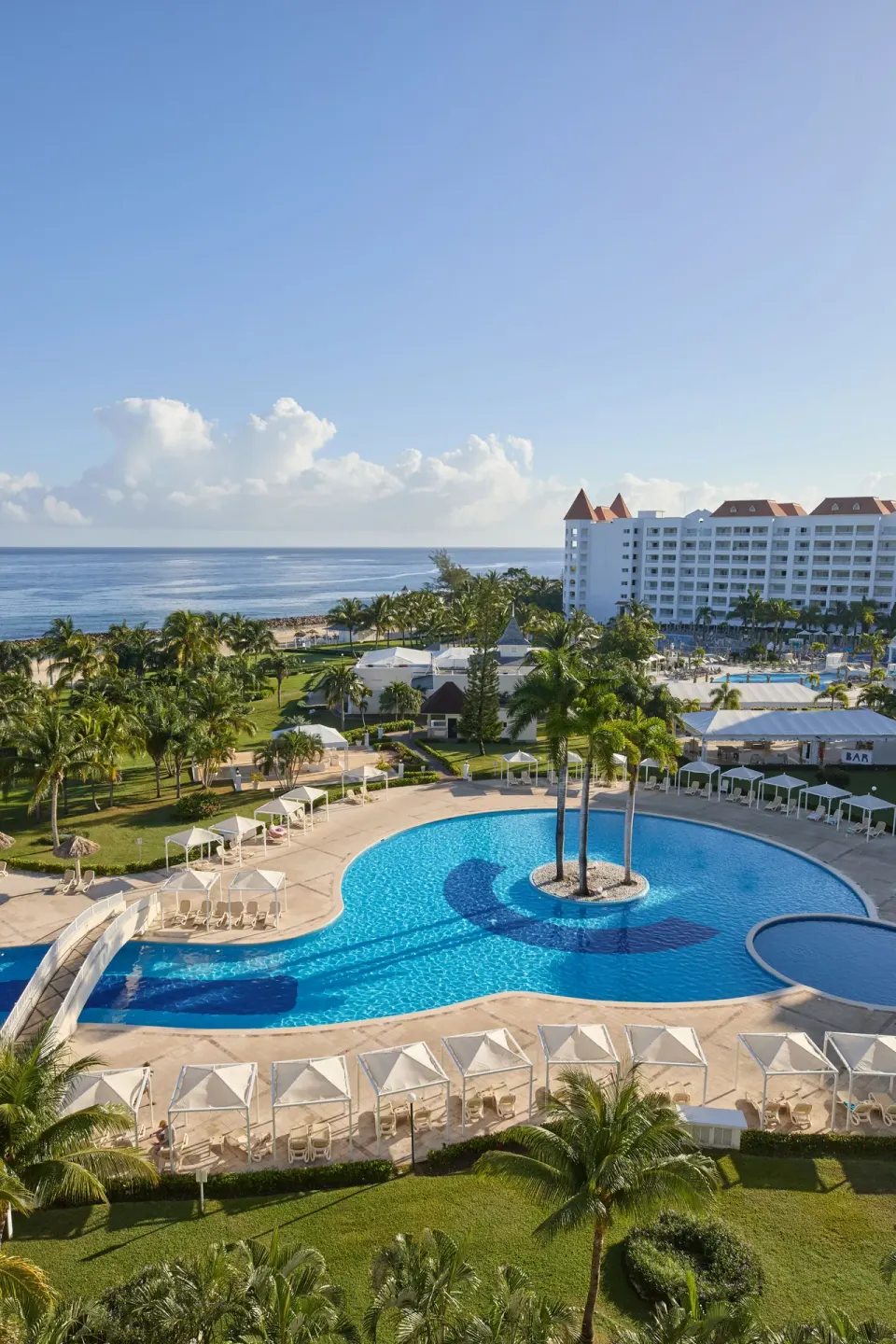 Large pool with cabanas, palms and ocean views at Bahia Principe Luxury Runaway Bay.