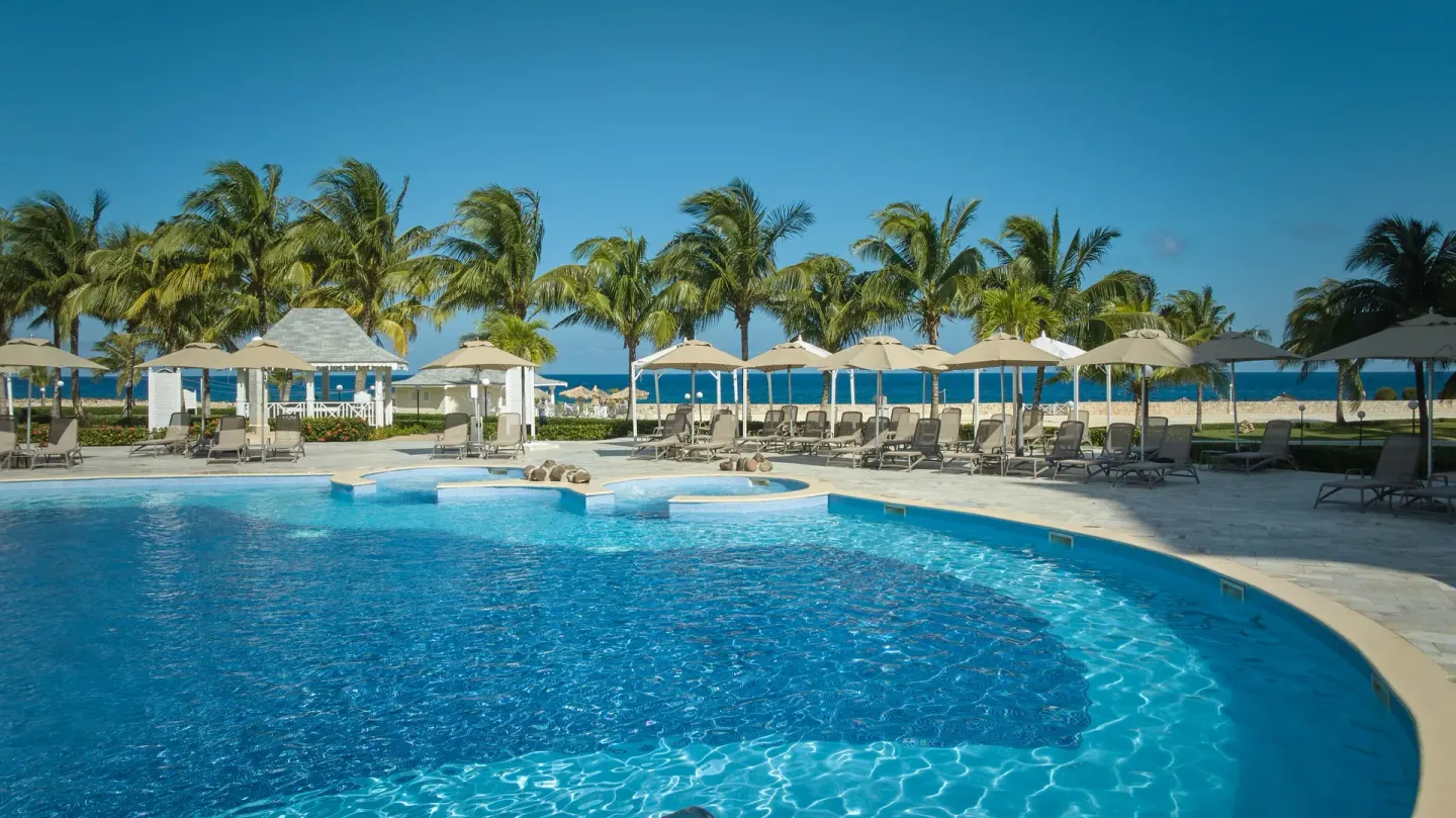 Pool deck with loungers, umbrellas, palms and ocean beyond at Bahia Principe Luxury Runaway Bay.