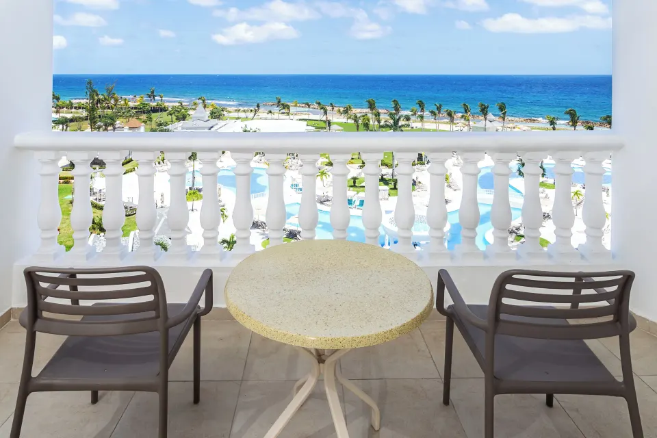 Junior Suite Sea View balcony with chairs overlooking pools and ocean at Bahia Principe Luxury Runaway Bay.