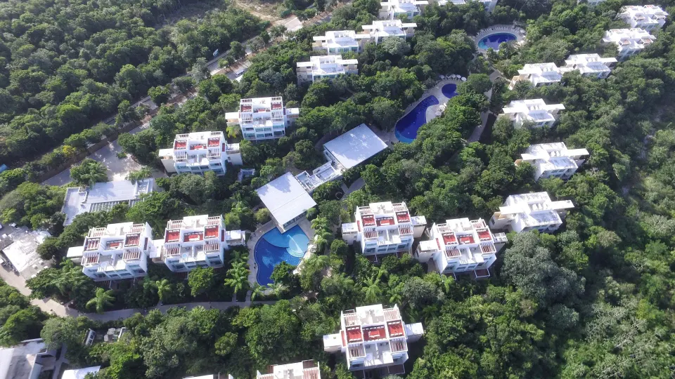 Aerial view of clustered white resort buildings and pools in forest at Bahia Principe Luxury Sian Ka'an