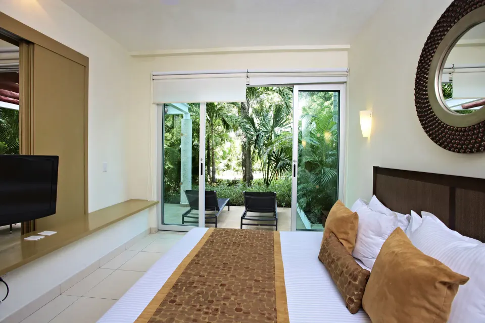 Bedroom with king bed and sliding glass door opening to a private patio and garden at Bahia Principe Luxury Sian Ka'an