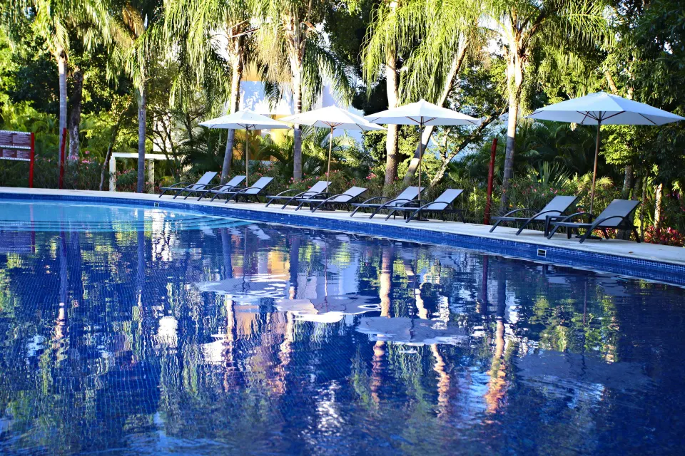 Pool surface reflecting umbrellas and trees with loungers along the deck at Bahia Principe Luxury Sian Ka'an