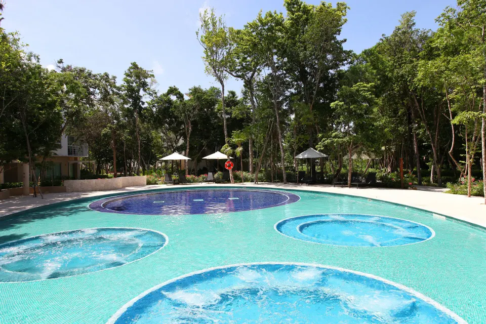 Outdoor pool with circular built-in whirlpool features surrounded by tropical trees at Bahia Principe Luxury Sian Ka'an