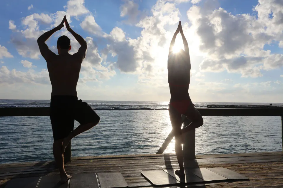 Two silhouetted people doing yoga on a wooden deck by the ocean at Bahia Principe Luxury Sian Ka'an