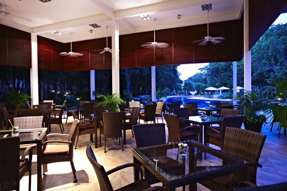 Covered evening poolside dining area with wicker chairs and ceiling fans at Bahia Principe Luxury Sian Ka'an