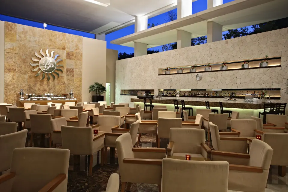 Evening view of a modern indoor restaurant and bar at Bahia Principe Luxury Sian Ka'an
