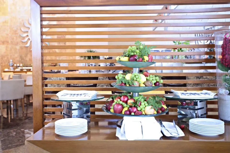 Buffet station with tiered fruit platters and plates in a resort dining area at Bahia Principe Luxury Sian Ka'an