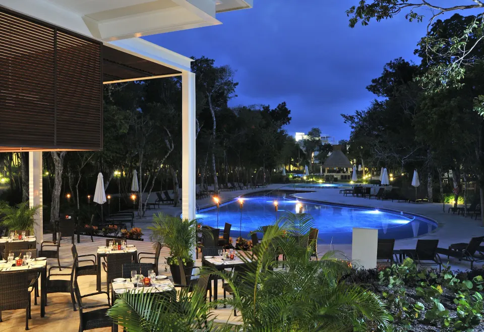 Night view of pool lit in blue with adjacent dining terrace at Bahia Principe Luxury Sian Ka'an